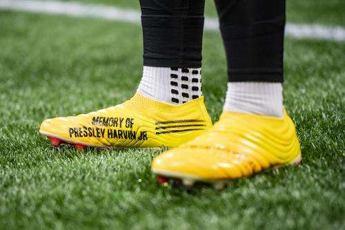 Pressley Harvin III standing in his yellow football cleats with "Memory of Pressley Harvin Jr" on the inside of the right cleat