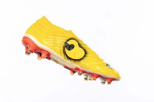 Yellow football cleat with a heart inside the outline of a kidney on the side