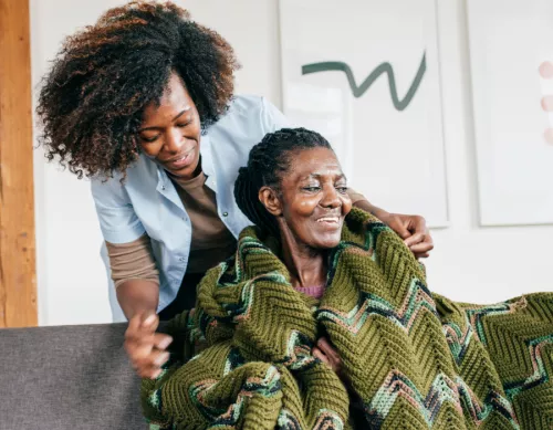 Black woman putting a blanket around the shoulders of another older Black woman