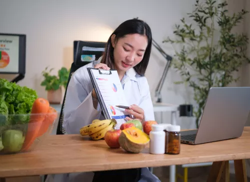 Dietitian consulting a client over a computer, holding up a clipboard