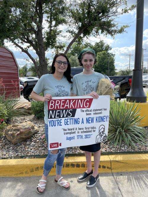 Savannah Stallbaumer and Katie Hallum holding a sign that reads, "Breaking News: you're getting a new kidney"