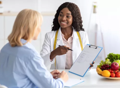 Black woman nutritionist reviewing information on clipboard with white woman patient