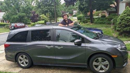 Ben Shlesinger posing through the sunroof of his gray van in his driveway