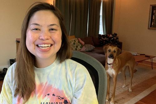 smiling woman sitting in chair wearing tie dye shirt with dog in background 
