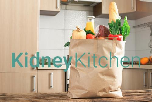 background of brown paper shopping bag filled with fresh vegetables with the words Kidney Kitchen written across image.