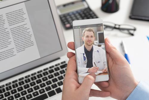 hands holding phone that has image of doctor during telehealth call