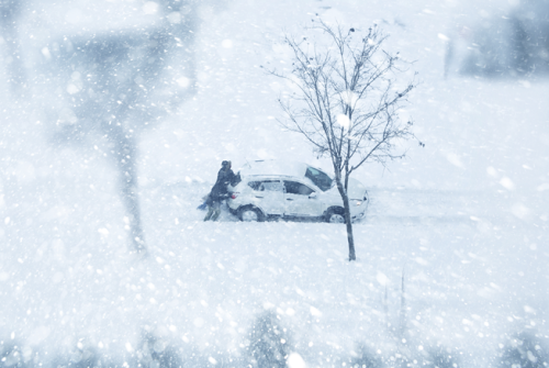 snowy scene with man wiping snow off car.