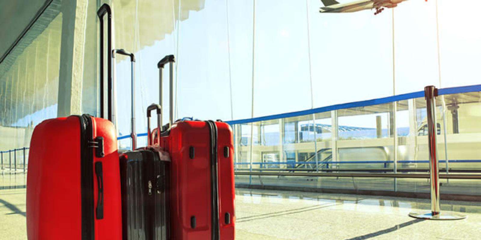 red suitcases standing with an airport with an airplane taking off in the background 